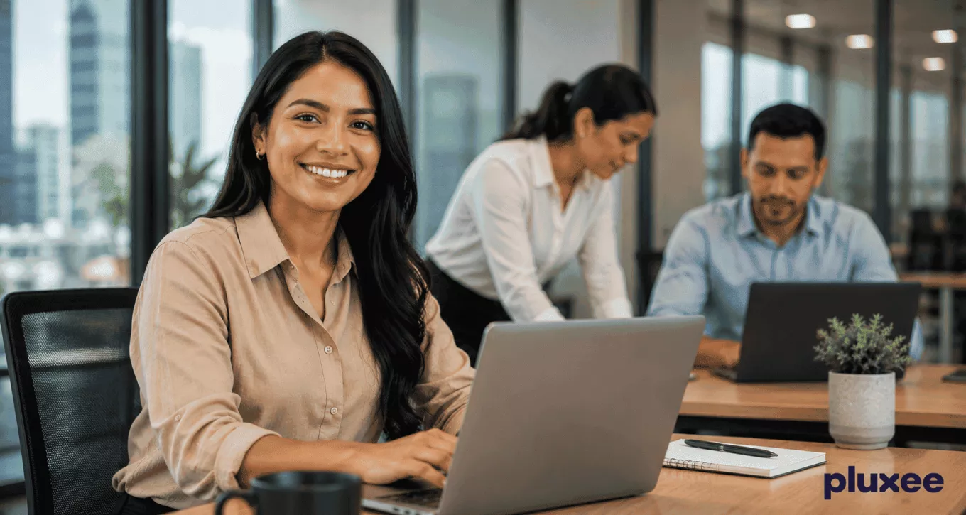 Mujer profesional sonriendo en su espacio de trabajo junto a su equipo, representando el compromiso laboral y la colaboración en la oficina