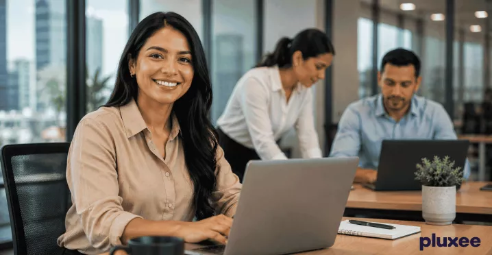 Mujer profesional sonriendo en su espacio de trabajo junto a su equipo, representando el compromiso laboral y la colaboración en la oficina