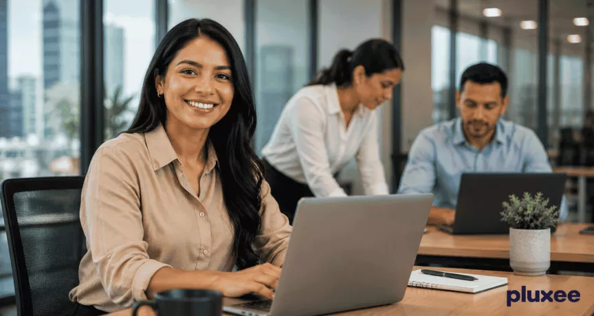 Mujer profesional sonriendo en su espacio de trabajo junto a su equipo, representando el compromiso laboral y la colaboración en la oficina
